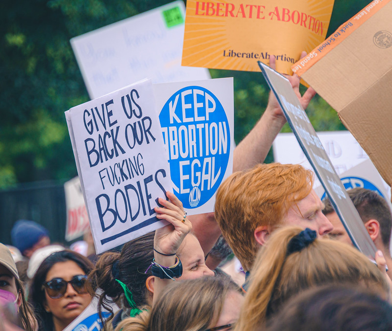 Protesters at a rally for abortion justice hold signs reading “Give us back our fucking bodies,” “Keep abortion legal,” and “Liberate Abortion.”