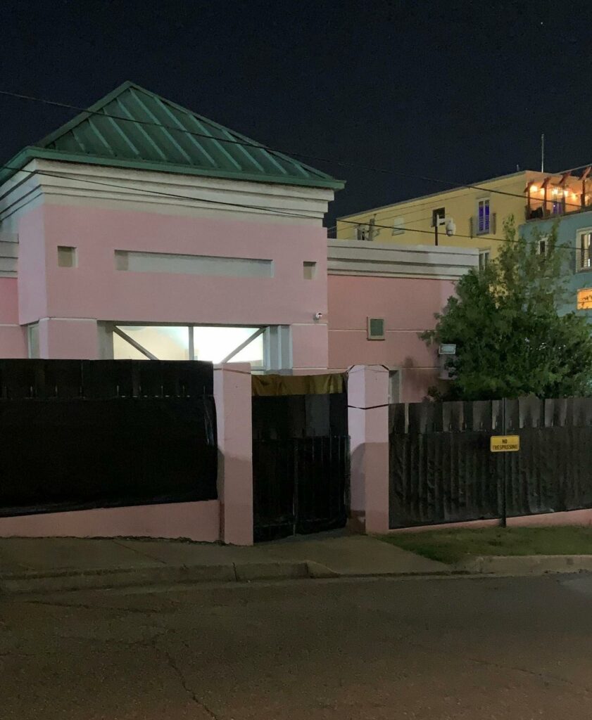 Light shines from the window of a pink house at night. The Pink House is the home of the Jackson Women’s Health Organization. The two-story house has a fence wrapped in black fabric.