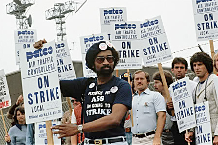 Strike PATCO workers in 1981, holding “On Strike” picket signs. One African-American worker at center of photo holding a picket and wearing a t-shirt that says: “Patience my ass. I am going on strike.”