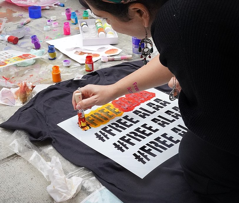 Mona Seif, sister of Alaa Abd el-Fattah, stencils a #FreeAlla t-shirt. This photo was taken during the ongoing encampment protest by Alaa's two sisters - Sanaa and Mona Seif - outside Britain's Foreign Office.