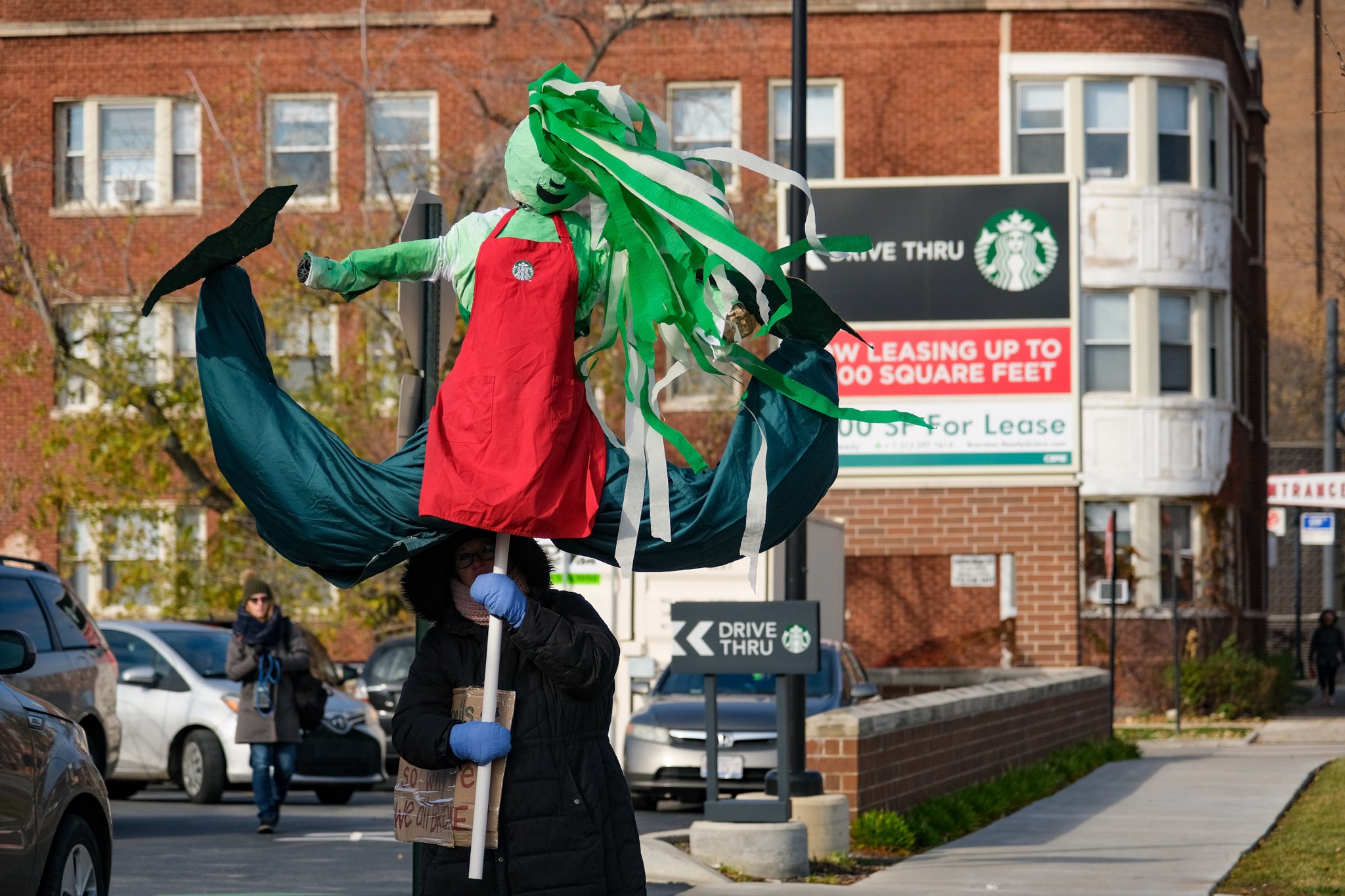 A worker in a Starbucks solidarity beanie holds a sign that reads, “UNION YES!” The “O” in “UNION” is the Starbucks Workers United logo, featuring a fist holding a coffee cup.