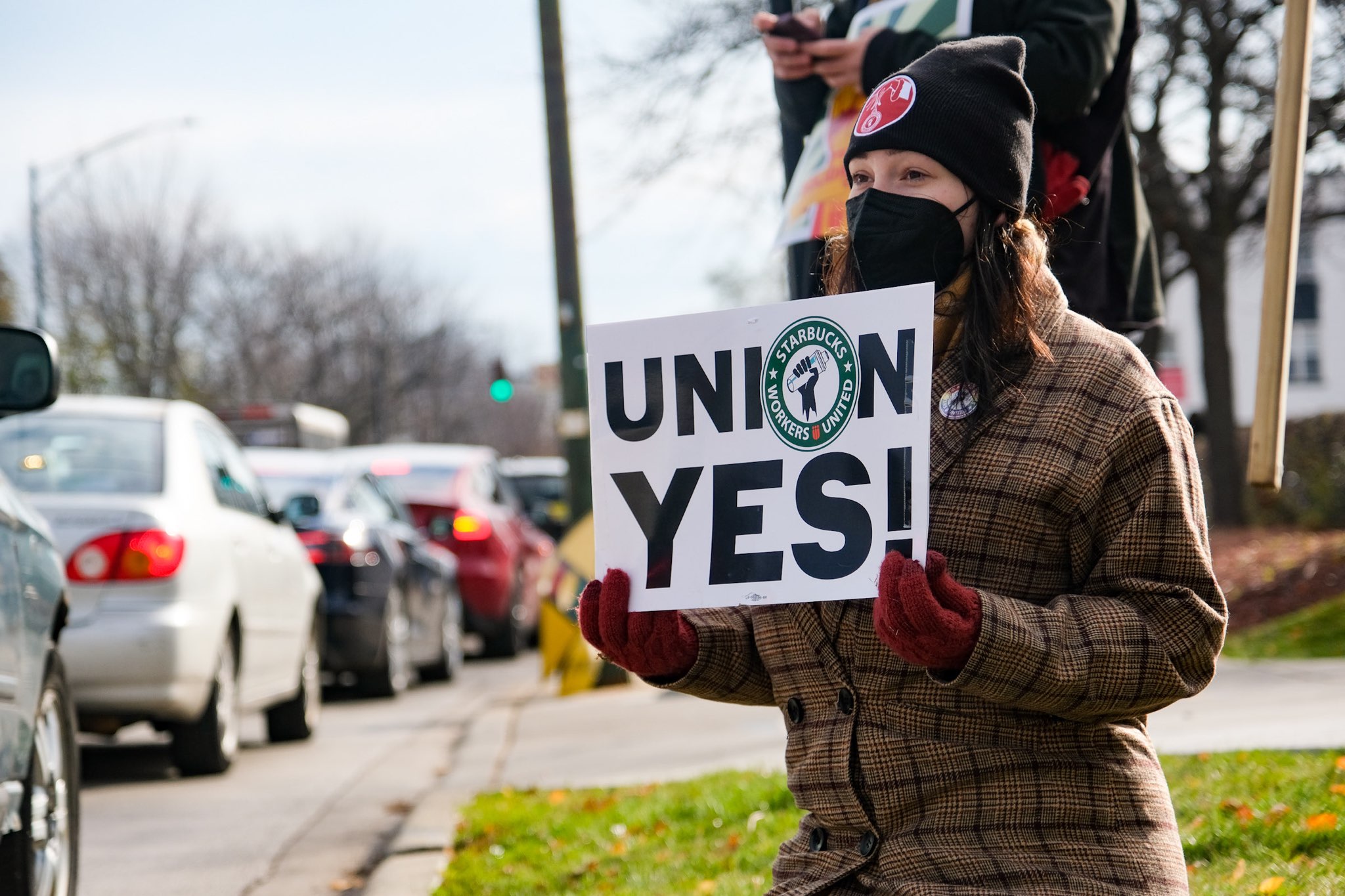 A person in heavy winter wear holds a sign reading Union Yes! in front of a line of cars.