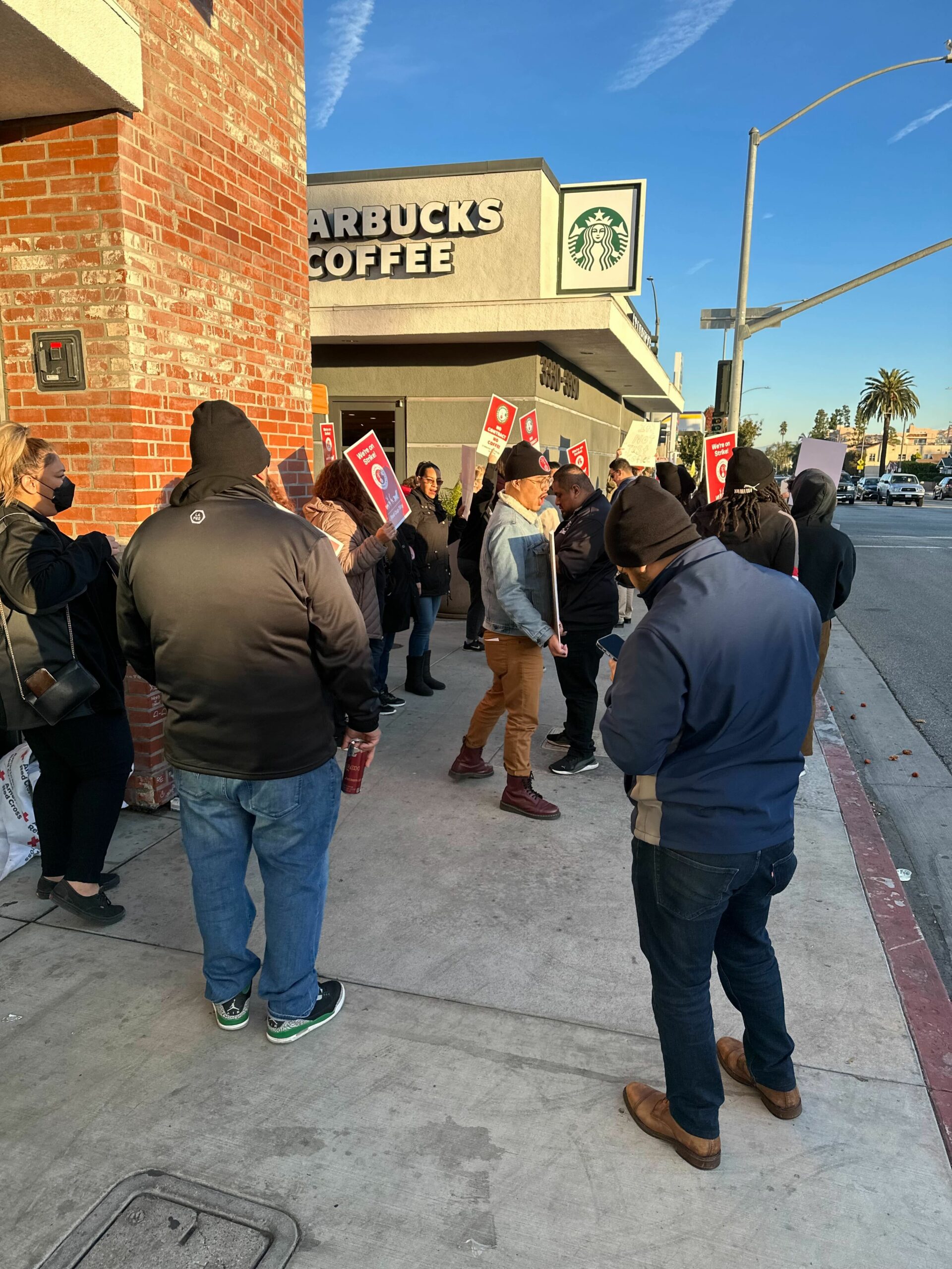Workers hold red picket signs and march in a circle outside a Starbucks store.