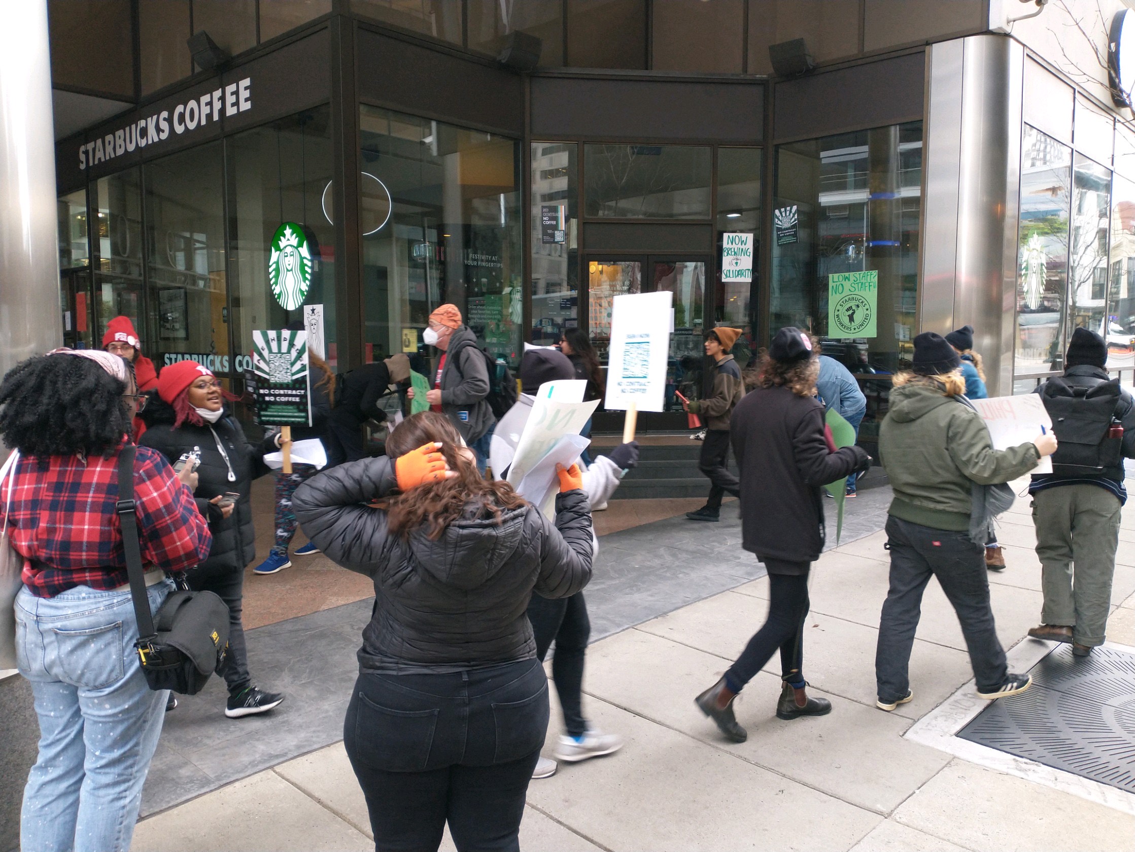 Starbucks workers hold picket signs and walk in a circle on the sidewalk in front of the entrance to the Starbucks on 20th and Market Street.