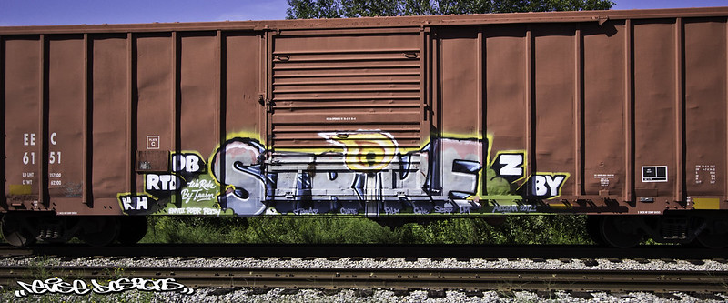 A red rust colored railway car, on its own on a railway track, with prominent graffiti reading, “Strike”, with the “i” in the shape of a lit match. 