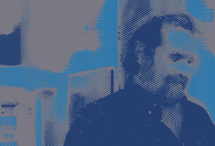 image in blue and black tones of scholar and socialist activist John Molyneux, a bearded older white man with glasses, wearing a button-down shirt.