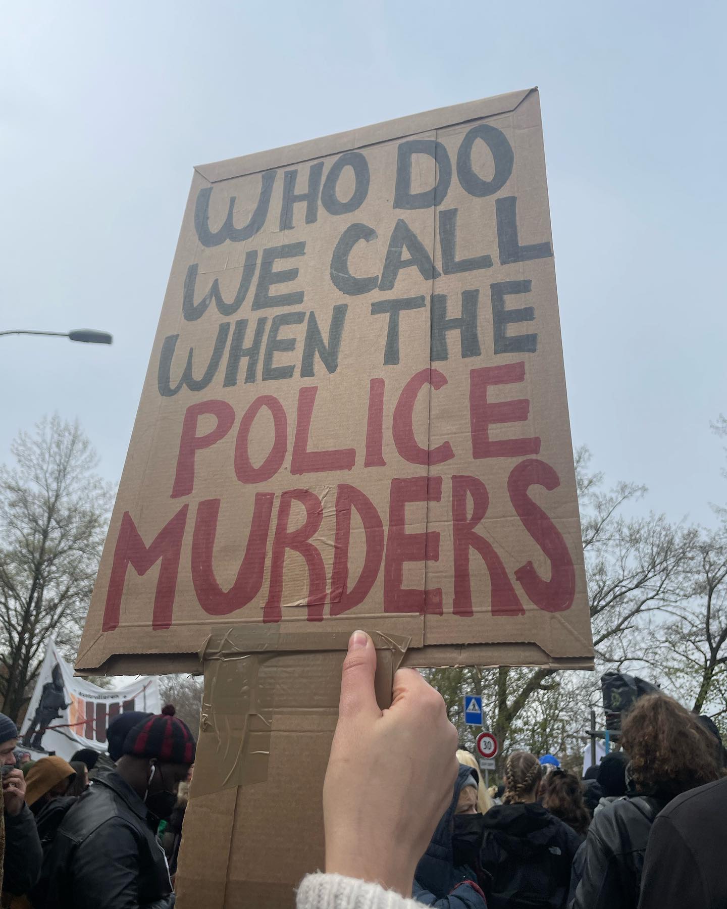 A white protestor in a sizable crowd at a demonstration against police violence in Lausanne, Switzerland last spring is holding a sign in English that asks the question “Who do we call when the police murders.”