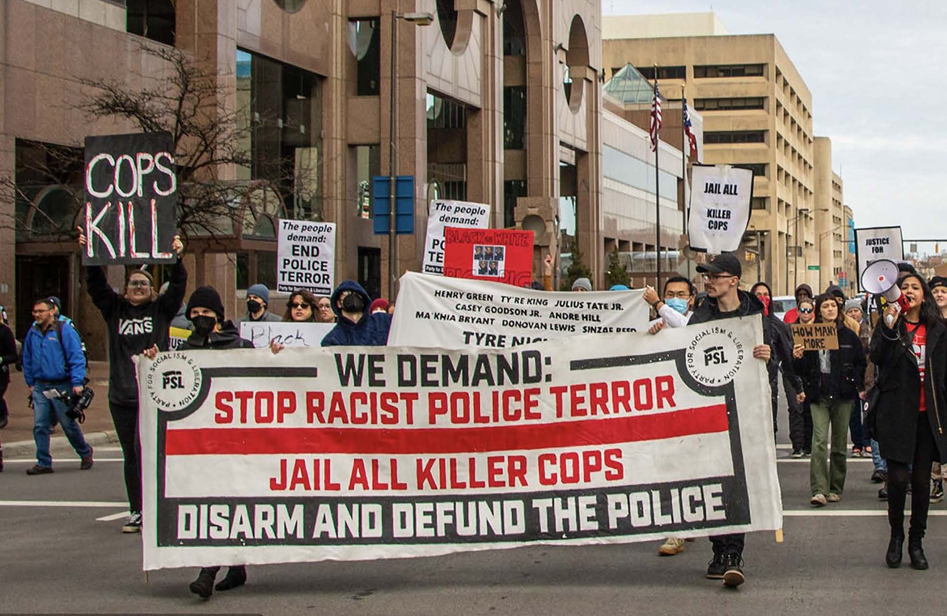Marches in a Columbus, Ohio event carry a banner reading "Stop Racist Police Terror, "Jail All Killer Cops" and "Disarm and Defund the Police" in red and black letters on a white background.