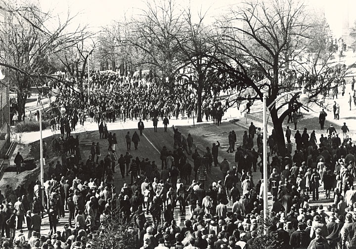 A large crowd gathers on a snow-covered lawn.