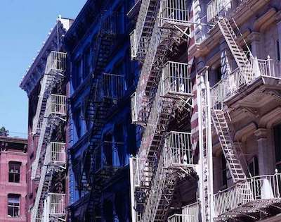 An image of white metal fire escapes climbing apartment buildings in New York.