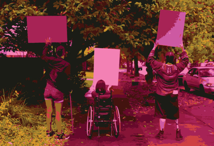 Three people hold up signs on a tree-lined street. One is standing with the assistance of a cane, one is in a wheelchair, and the third is apparently unassisted.