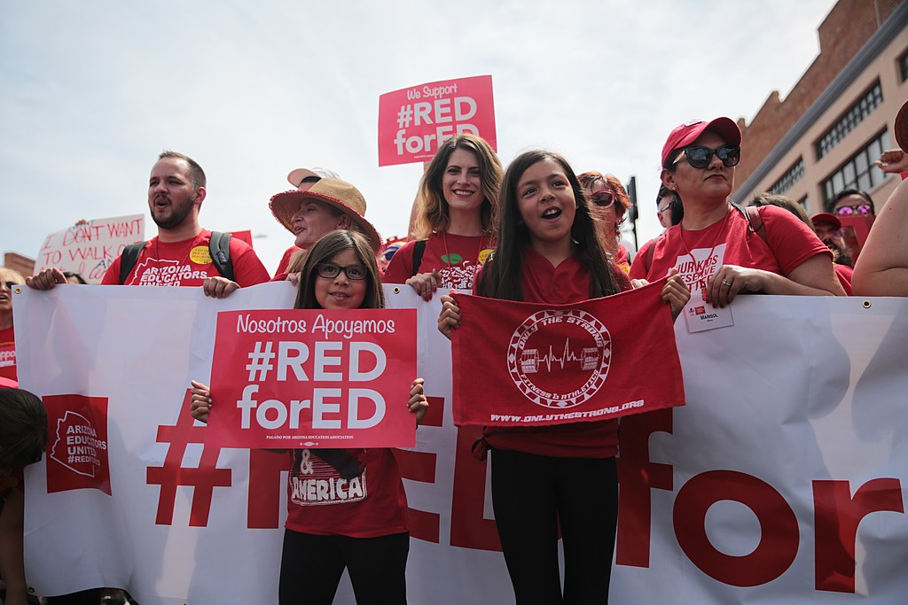 About twelve people are gathered holding signs reading "Red for Ed"