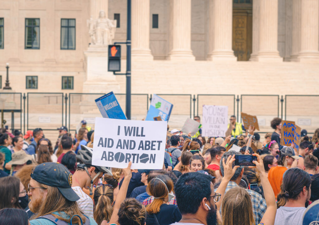 A group of young people at a demonstration; one prominent sign reads, I will aid and abet abortion.