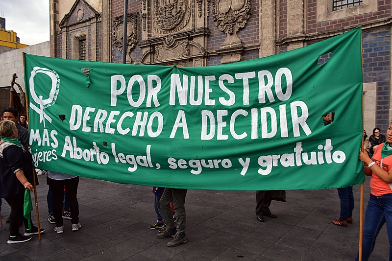 A green banner with white writing has a women's symbol and the words Por Nuestro Derecho a Decidir (for Our Right to Decide)