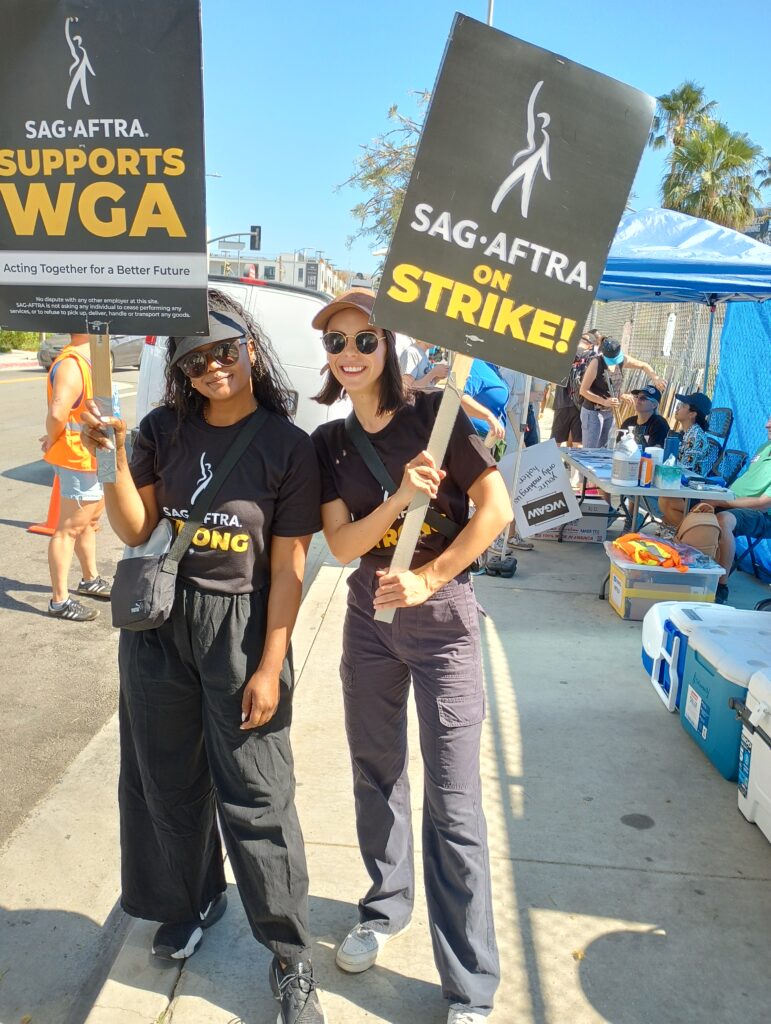 Two women hold picket signs for WGA and SAG-AFTRA reading Strike!