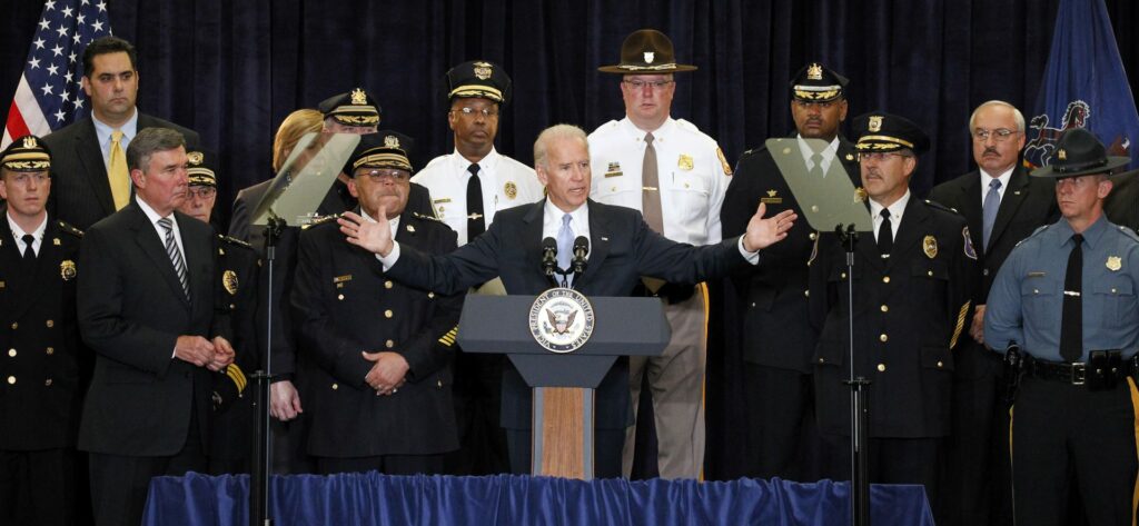 President Joe Biden stands behind a podium flanked by a dozen police officers in uniform.