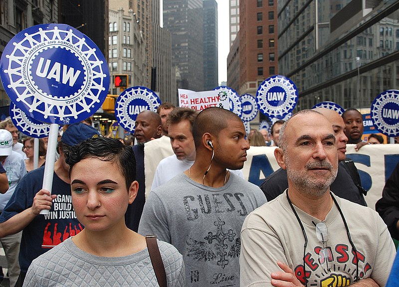 A group of walking people hold signs reading UAW on a city street during a climate protest march.