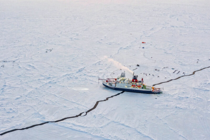 A boat straddles a crack in an iced-over body of water.