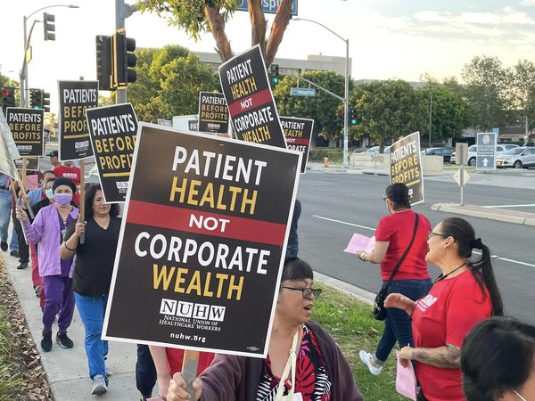 A dozen people march a picket line with signs reading Patient Health not Corporate Wealth.