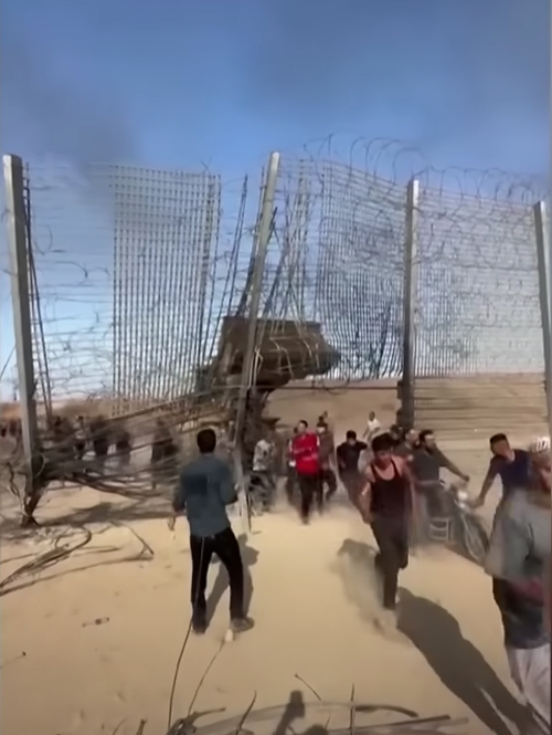 Palestinians run—and ride motorbikes—through a breach in a razor-wire fence constructed to shut them into Gaza. The front-end loader that broke through the barrier is visible in the background, on the Gaza side of the fence.