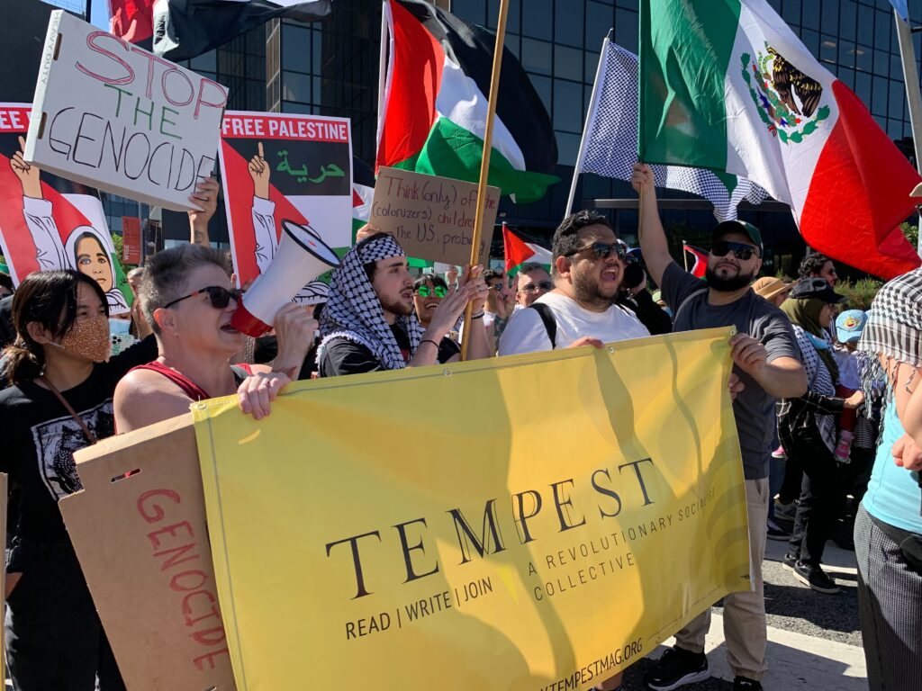 Several people march behind a yellow banner reading Tempest: A Revolutionary socialist collective. One is speaking in a megaphone. Others wave Palestinian and Mexican flags. Signs read Stop the Genocide and Free Palestine.