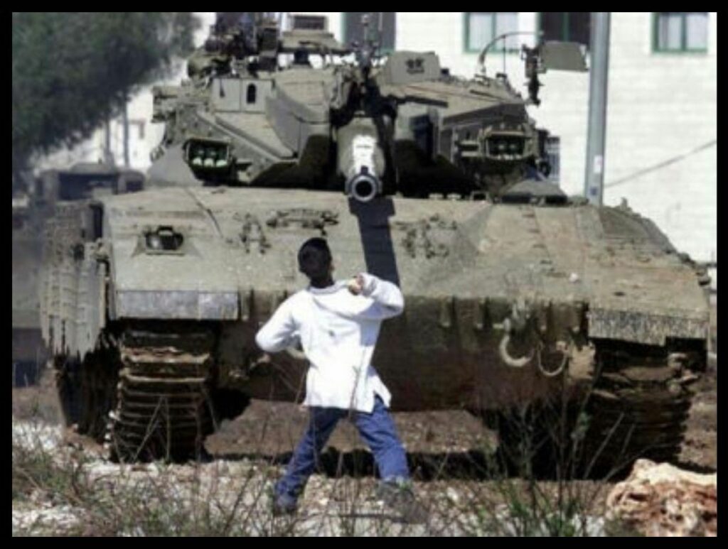 A boy in a white shirt and blue pants prepares to throw a rock at a tank bearing down on him. It is Faris Odeh, shot dead in 2000 during the Al-Aqsa Intifada.