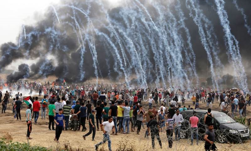 Tear gas rains down on a crowd of protesters in a field.