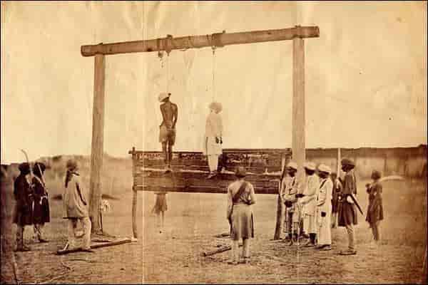 Photo shows two suspected participants in the 1857 Indian Rebellion hanging from a gallows, at an unknown location, surrounded by nine Indian soldiers.