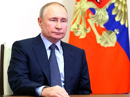President of Russia Vladimir Putin during the meeting with permanent members of Security Council in December 2022. He is frowning, seated in a blue suit in front of a Russian flag.