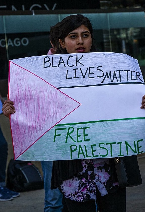Protester holding a hand made sign of the Palestinian flag with hand written message across the flag that reads: Black Lives Matter at the top, and “Free Palestine” at the bottom.